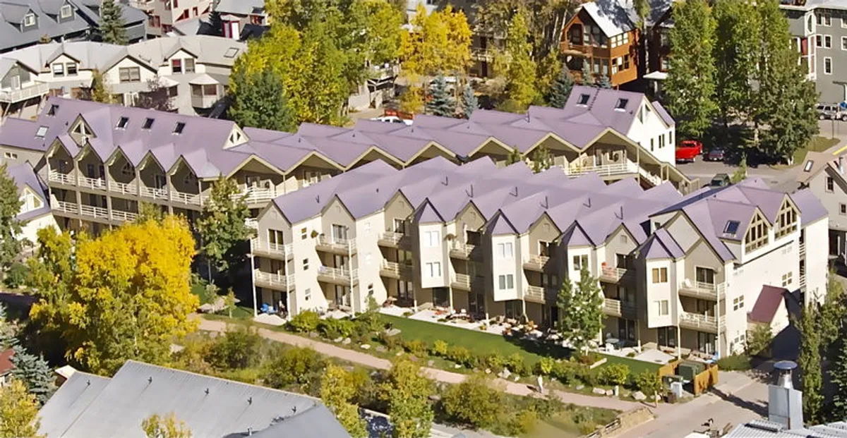 Exterior view of a modern residential building surrounded by lush greenery, showcasing balconies with outdoor seating. The garden area invites gatherings or relaxation, while the balconies hint at opportunities for outdoor dining and enjoying the environment.