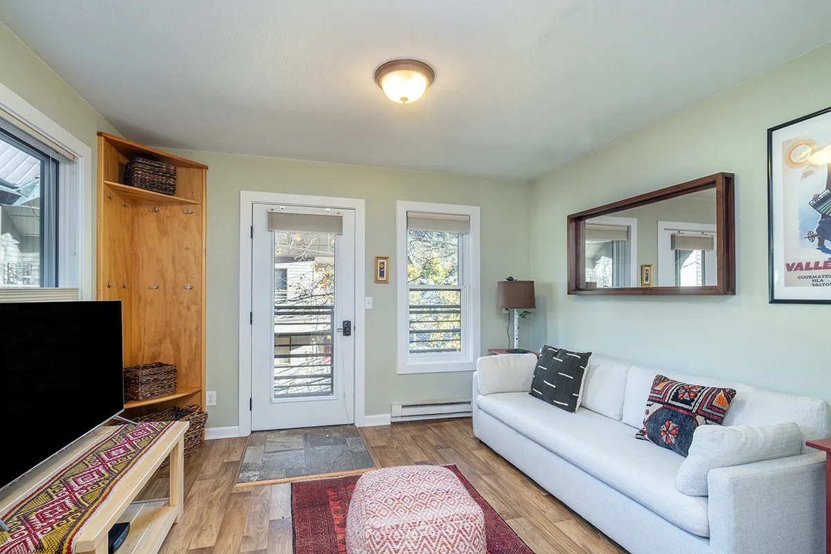 A cozy living area featuring a plush sofa, coffee table, flat-screen television, and large windows letting in natural light. The room is styled with inviting decor and creates a comfortable setting for families to gather, relax, or watch their favorite shows together.