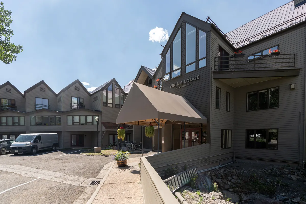 An exterior image featuring the Viking Lodge sign, entrance awning, large windows, and surrounding greenery. The scene feels welcoming and hints at the convenience and community atmosphere of the property, set near trailheads and the river.
