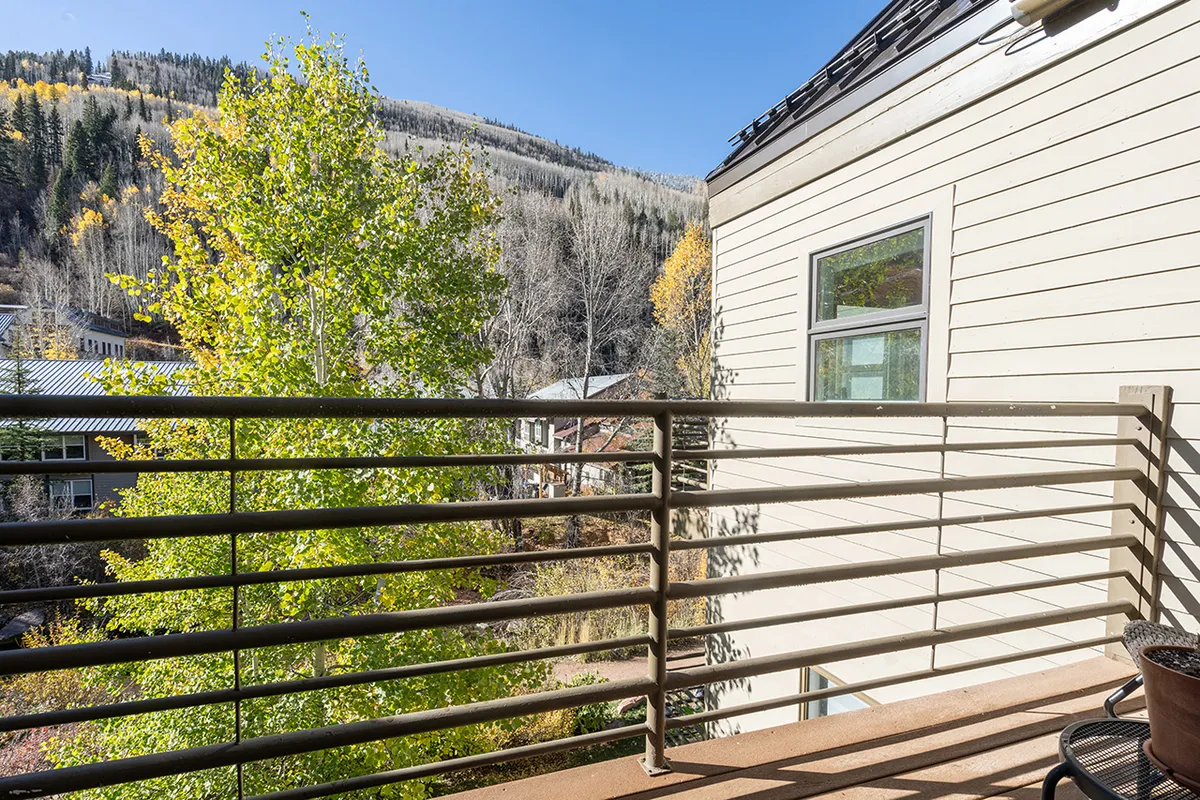 A tranquil balcony with a sturdy railing overlooks lush trees and a distant mountain backdrop. The space is perfect for sitting with a cup of coffee, breathing in fresh air, and absorbing peaceful natural views. The image captures the coveted private outdoor space mentioned in the section, and highlights river and peak vistas.