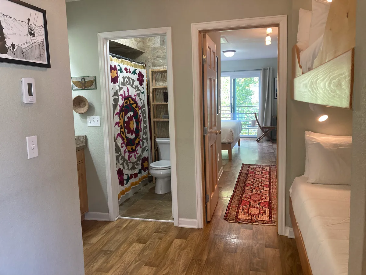 An inviting interior with colorful touches, showing bunk beds, a glimpse of the living space, wooden shelving, and a playful rug. The image emphasizes the lively and comfortable mood, with areas for both relaxation and togetherness.